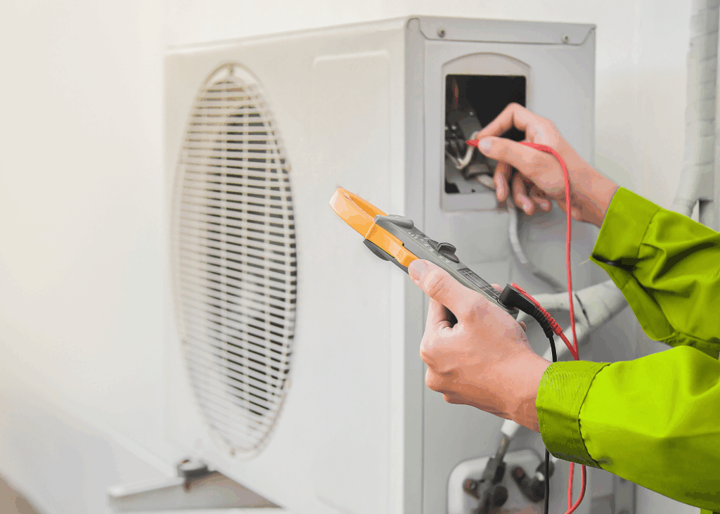 A person is servicing an air conditioner, examining the components with a screwdriver.