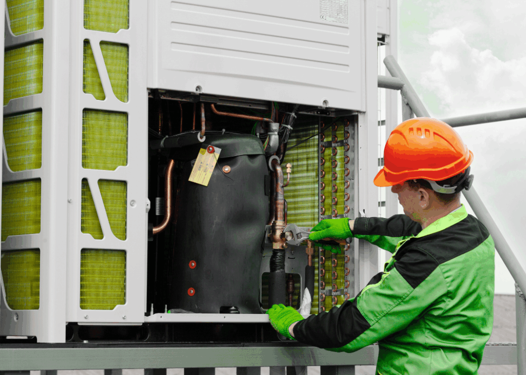 An individual works on an air conditioning unit, adjusting parts while seated on the floor.